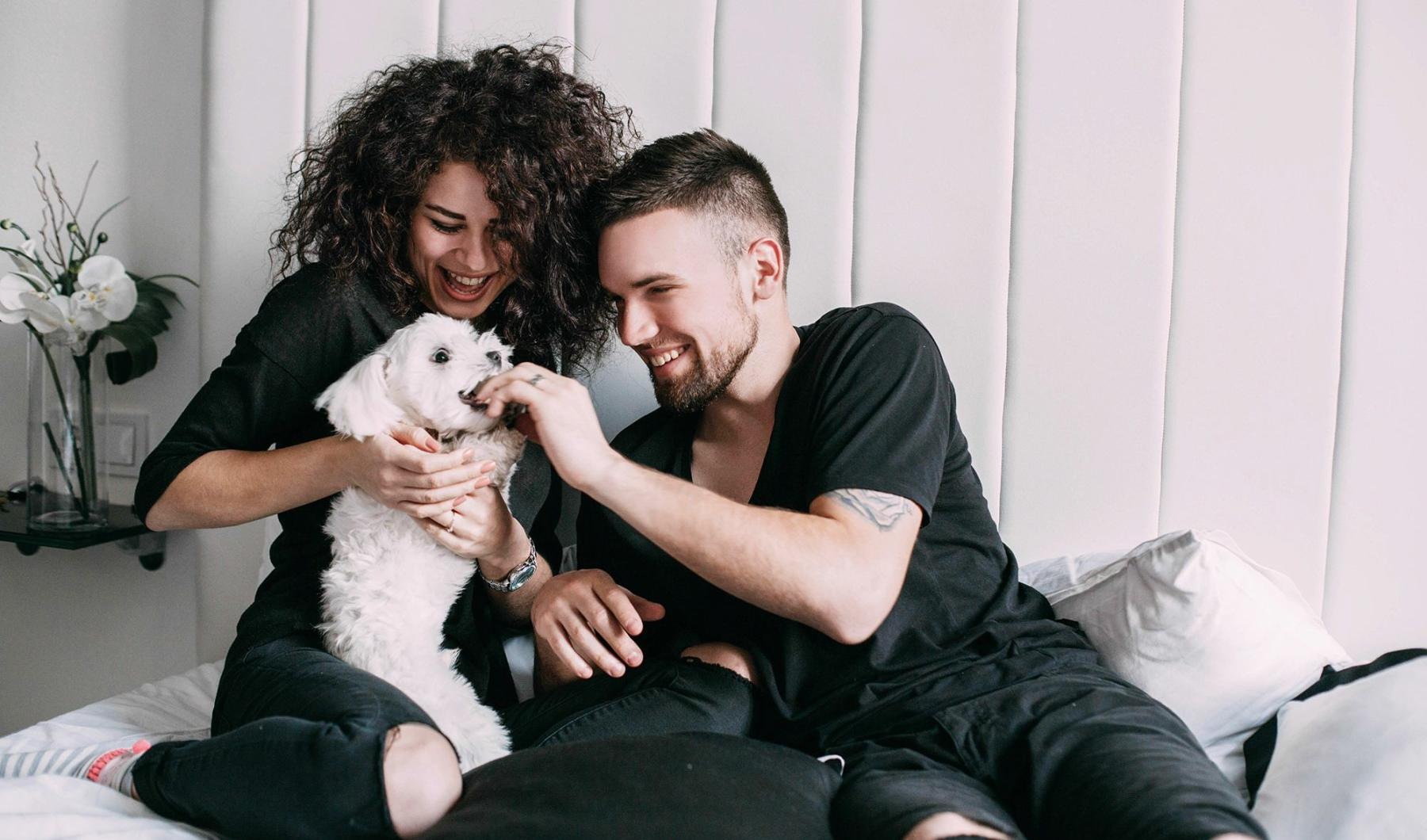 a man and woman sitting on a bed playing with a dog