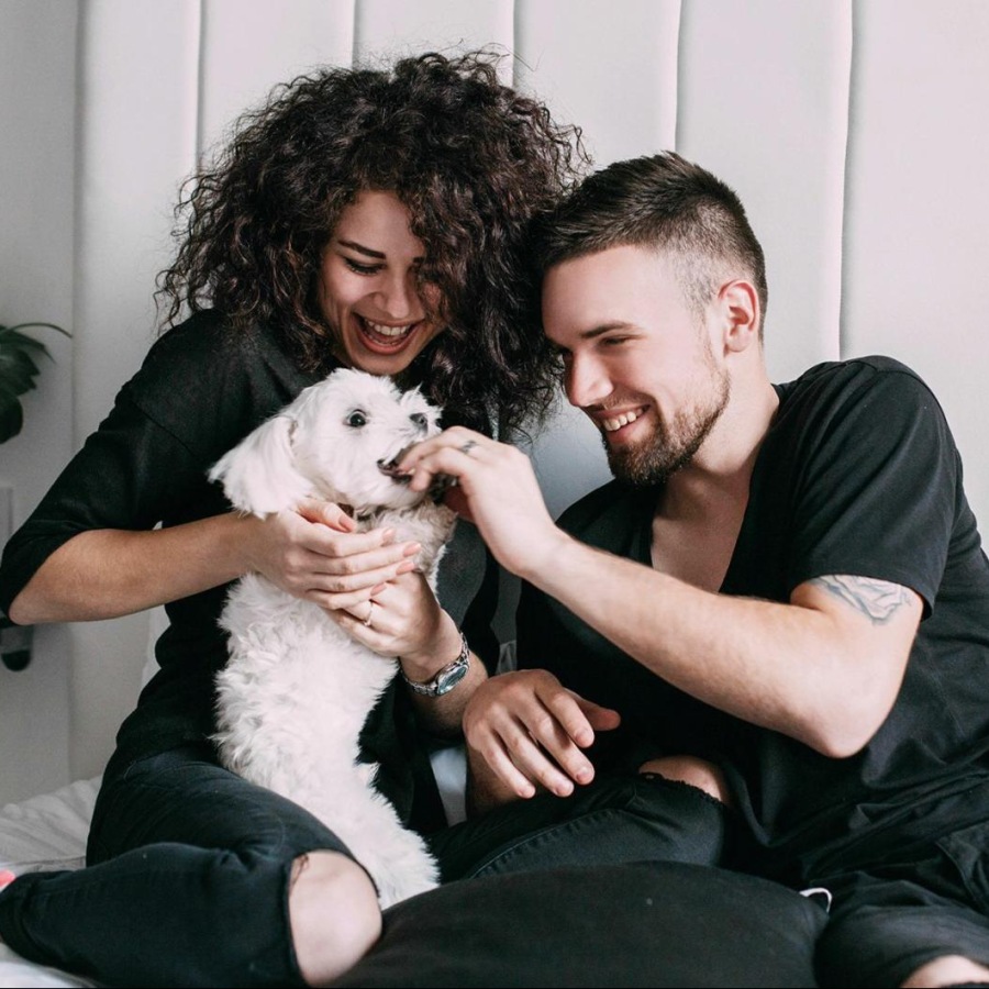 a man and woman sitting on a bed playing with a dog