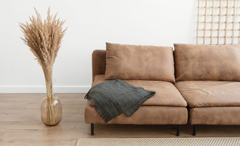 living room with a throw on a couch beside a large floor vase with a plant in it