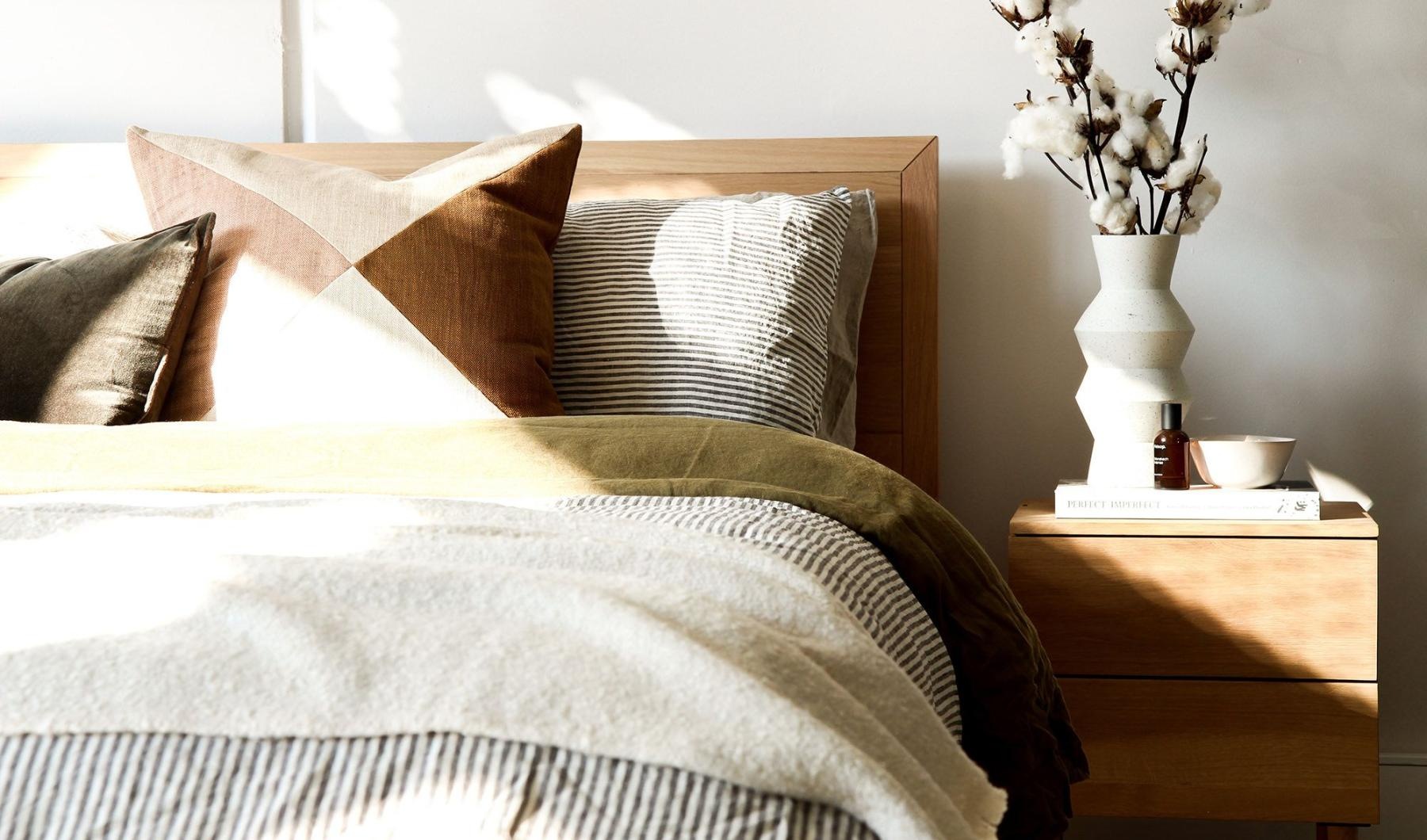 swath of sunlight shines across a well made bed and bedside table with a vase of cotton plants